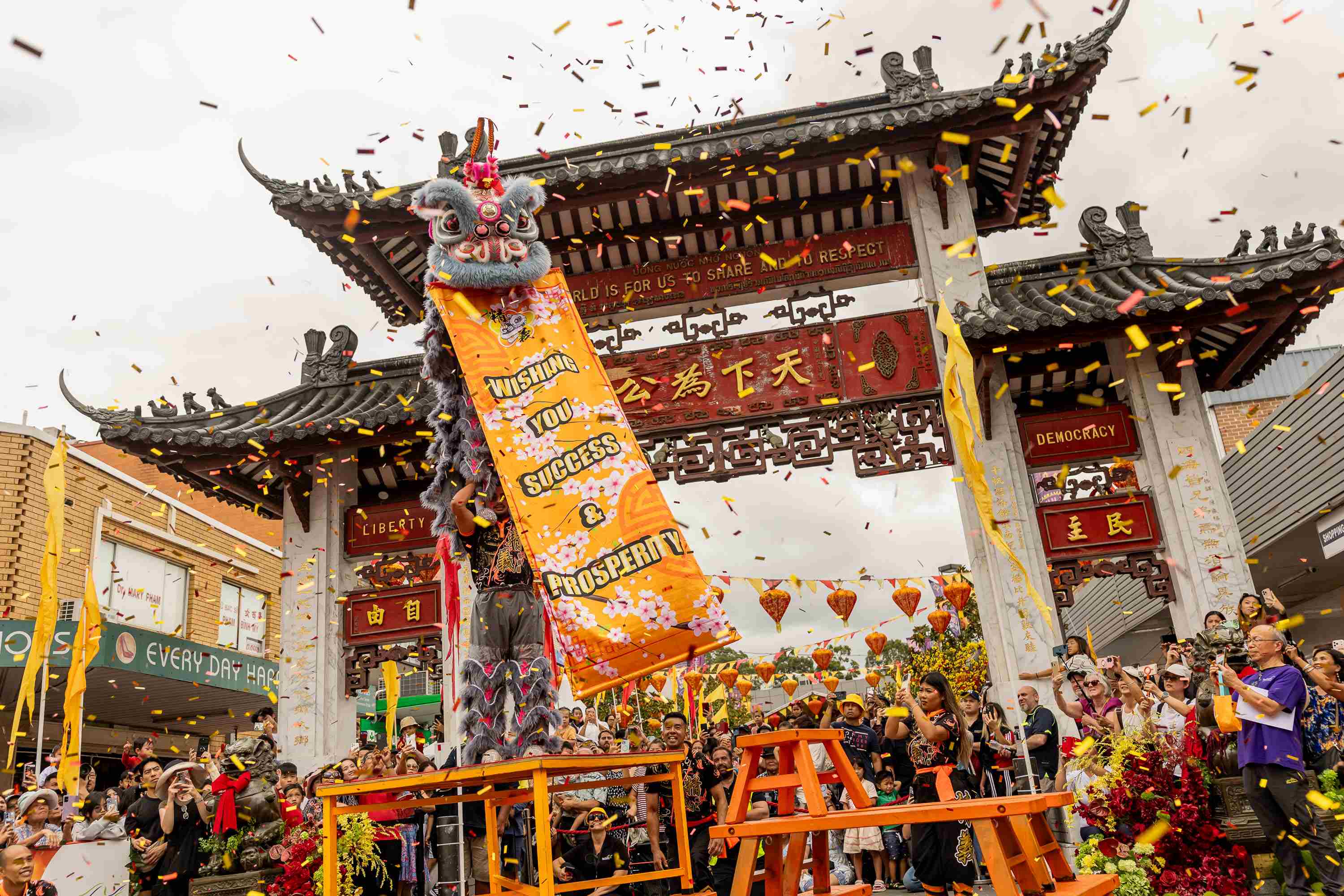 Lion dancer holding Happy New Year sign at front of Pai Lau Gate at 2026 Cabramatta Lunar New Year.